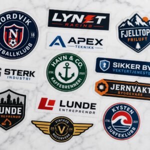 Flatlay av skreddersydde DTF-transfermerker i ulike former og størrelser på hvit overflate — logoer, tekst og emblemer på transparent PET-film